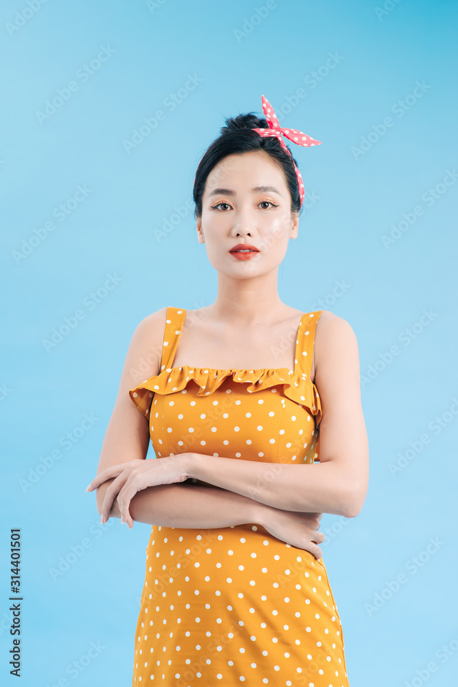 Fashionable graceful Young woman posing on blue background. Romantic adorable girl in polka dot yell