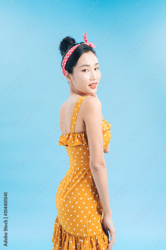 Fashionable graceful Young woman posing on blue background. Romantic adorable girl in polka dot yell