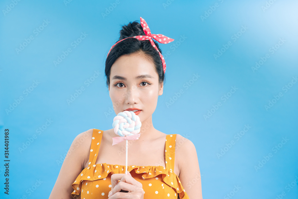 Attractive young woman in a yellow dress with white dots holding a bright Lollipop in her hand on bl