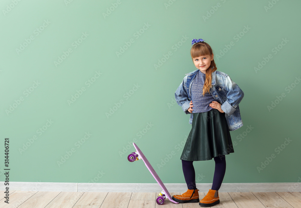 Cute fashionable girl with skateboard on color background