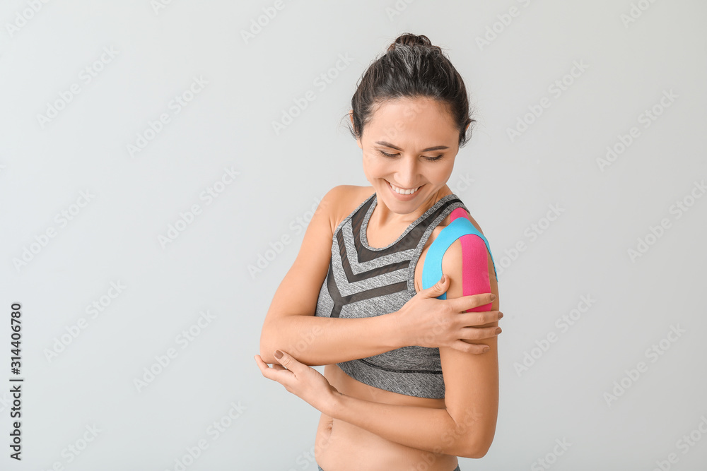 Sporty woman with physio tape applied on shoulder against light background