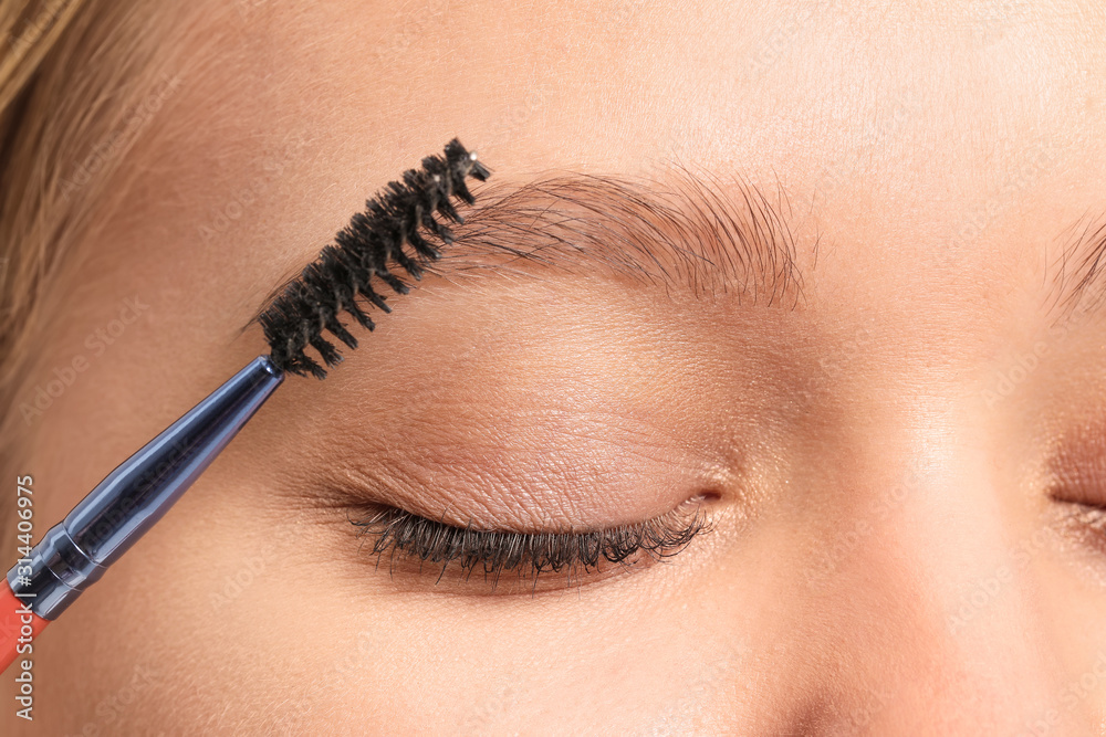 Young woman correcting shape of her eyebrows, closeup