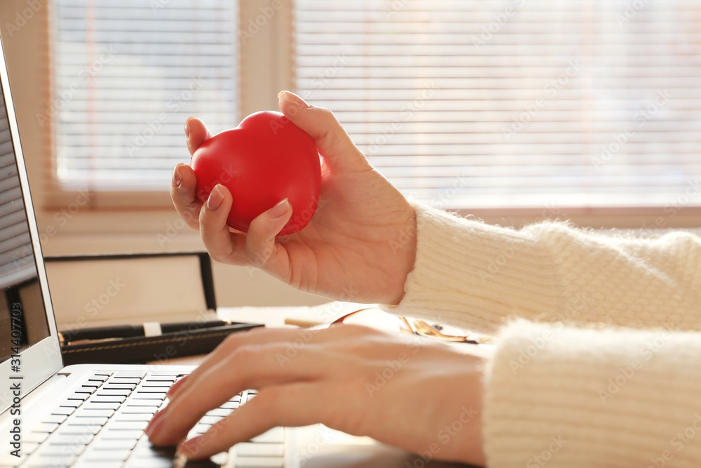 Woman squeezing stress ball while working with laptop in office