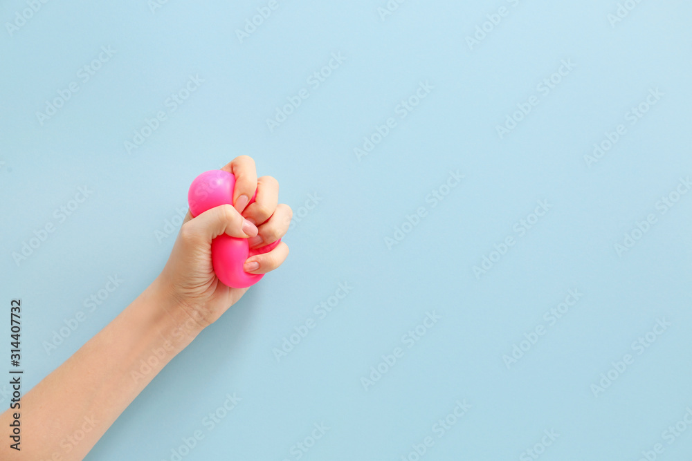 Female hand squeezing stress ball on color background