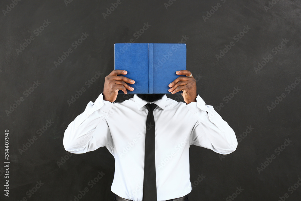 African-American teacher with book near blackboard in classroom