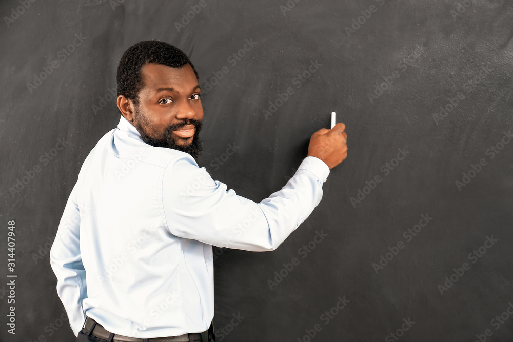 African-American teacher writing on blackboard in classroom