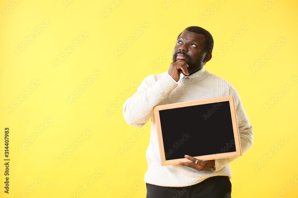 Thoughtful African-American teacher with chalkboard on color background