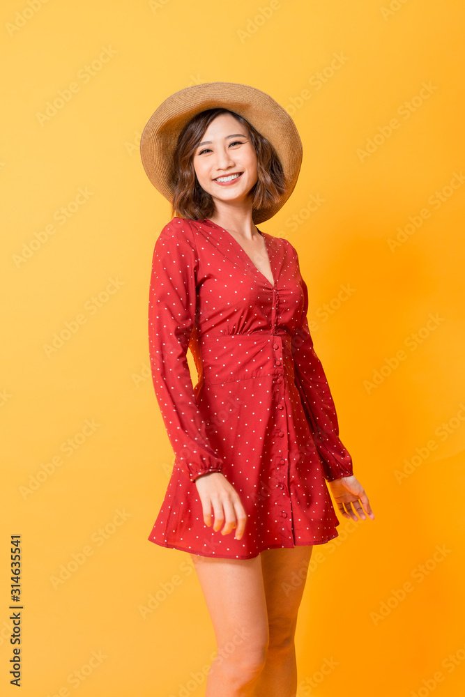 Portrait of young beautiful asian woman  wear red dress and hat over orange background. Summer conce