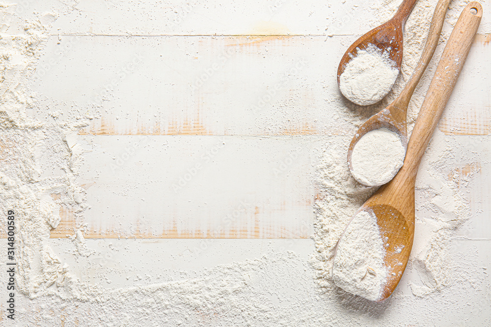 Scattered flour and spoons on white wooden background