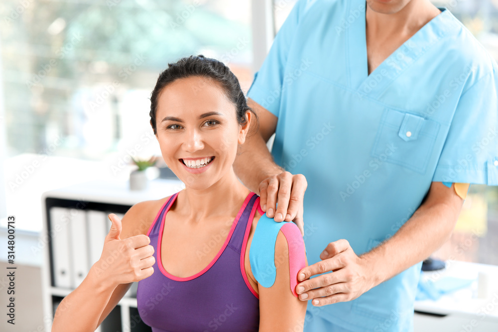 Physiotherapist applying tape onto womans shoulder in clinic