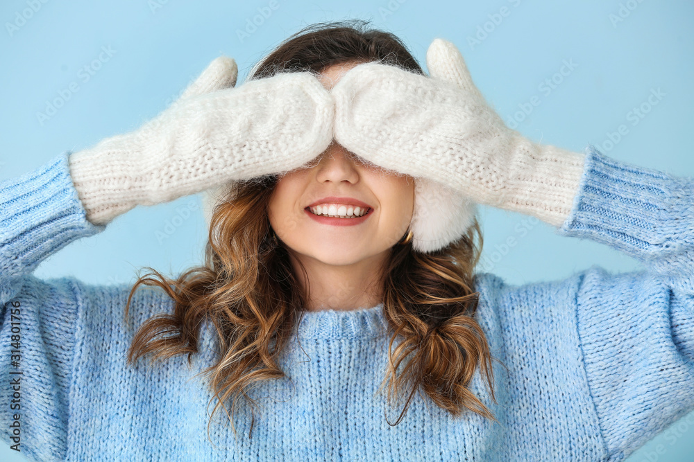 Beautiful young woman in warm sweater and mittens on color background