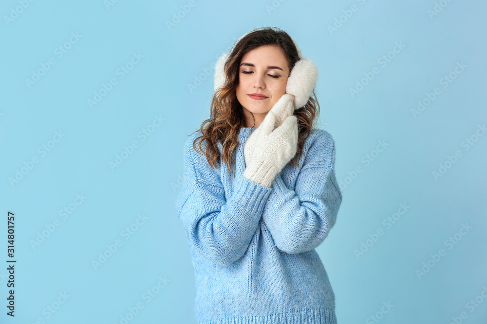 Beautiful young woman in warm sweater and mittens on color background