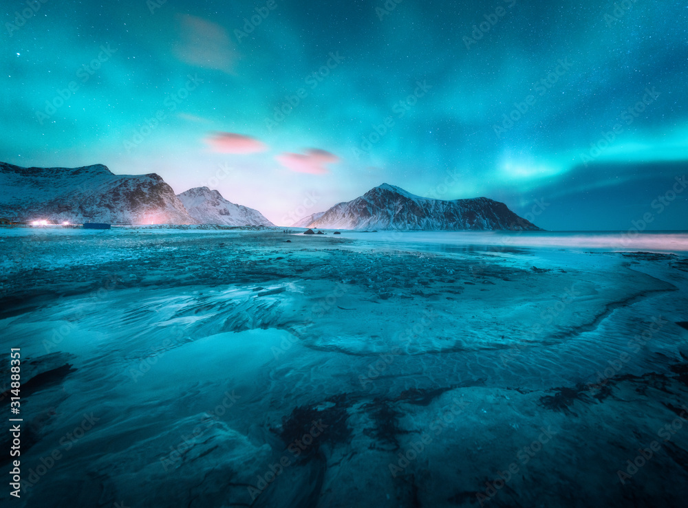 Aurora borealis above the snowy mountain and sandy beach in winter. Northern lights in Lofoten islan