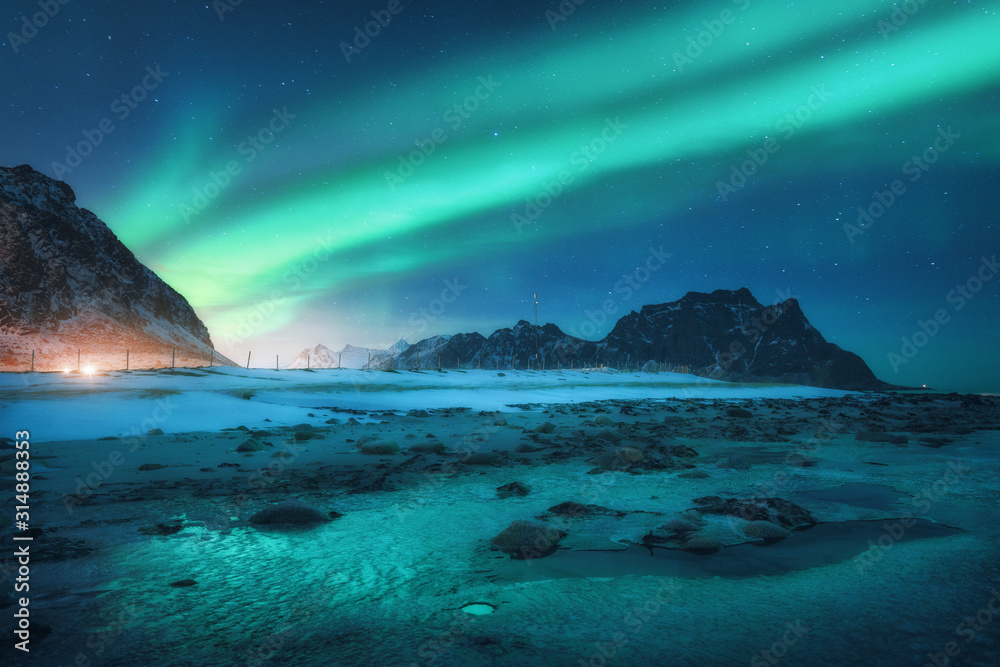 Aurora borealis above the snowy mountain and sandy beach in winter. Northern lights in Lofoten islan