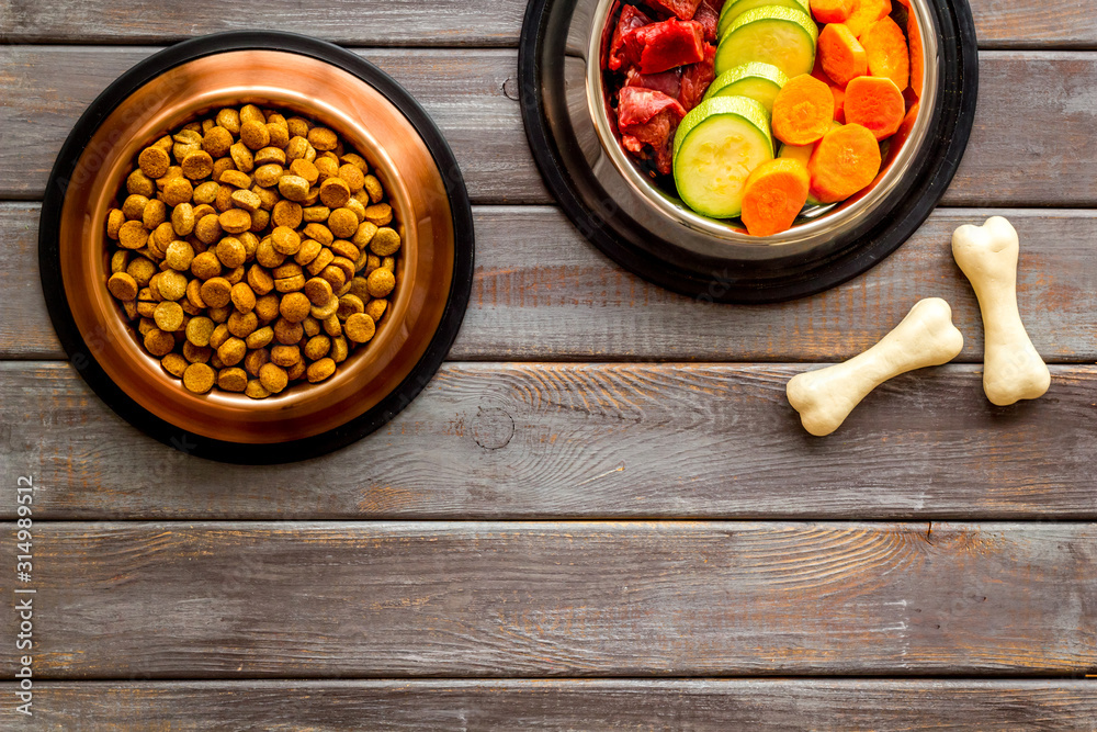 Ingredients of dry feed for dogs - meat, vegetables - near bones on dark wooden background top view 