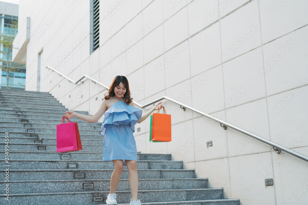 快乐的亚洲女孩走下楼梯，对自己的购物感到满意