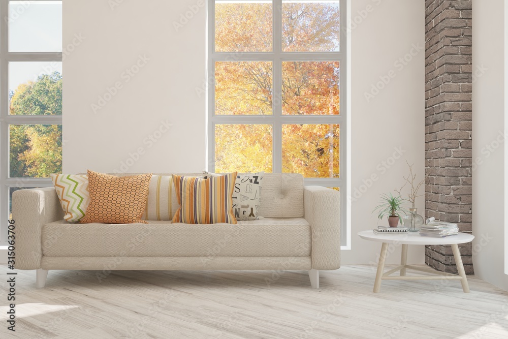 Stylish room in white color with sofa and autumn landscape in window. Scandinavian interior design. 