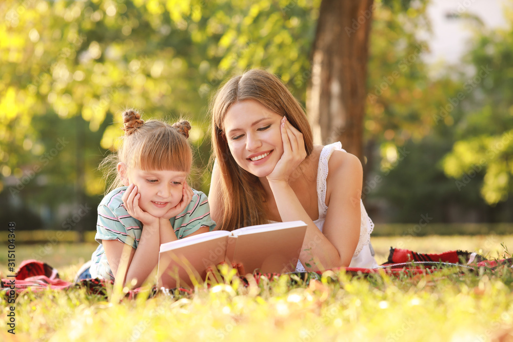 Beautiful young woman and her little daughter reading book in park