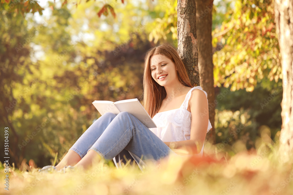 Beautiful young woman reading book in park