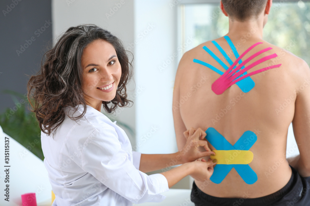 Physiotherapist applying tape onto mans back in clinic