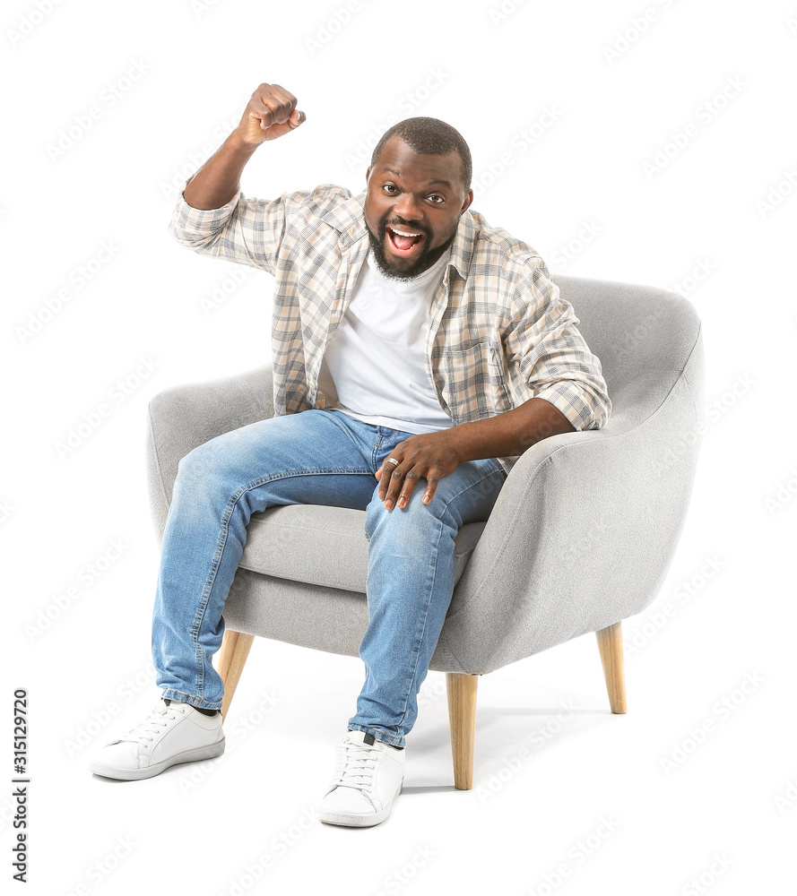 Emotional African-American man watching TV while sitting in armchair against white background