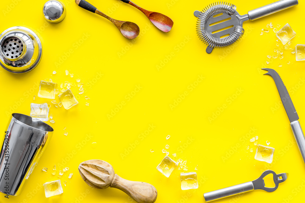 Bar utensil, tools - shaker, stainer - near ice cubes on yellow background top-down frame copy space