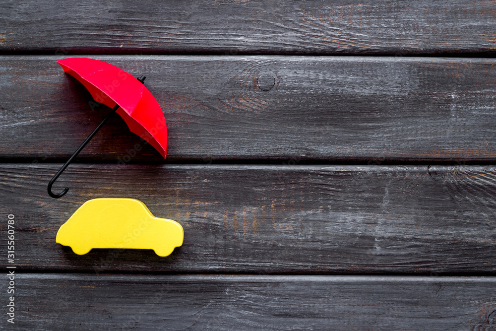 Car insurance. Automobile toy under umbrella on dark wooden background top-down copy space