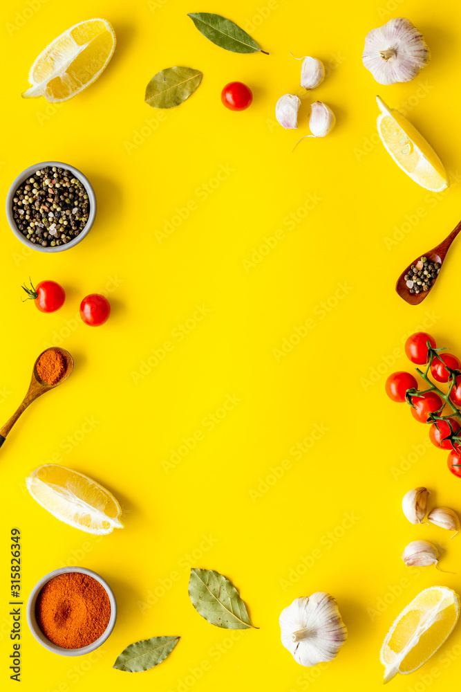 Kitchen frame with spices and food - pepper, garlic, cherry tomatoes - on yellow background top-down