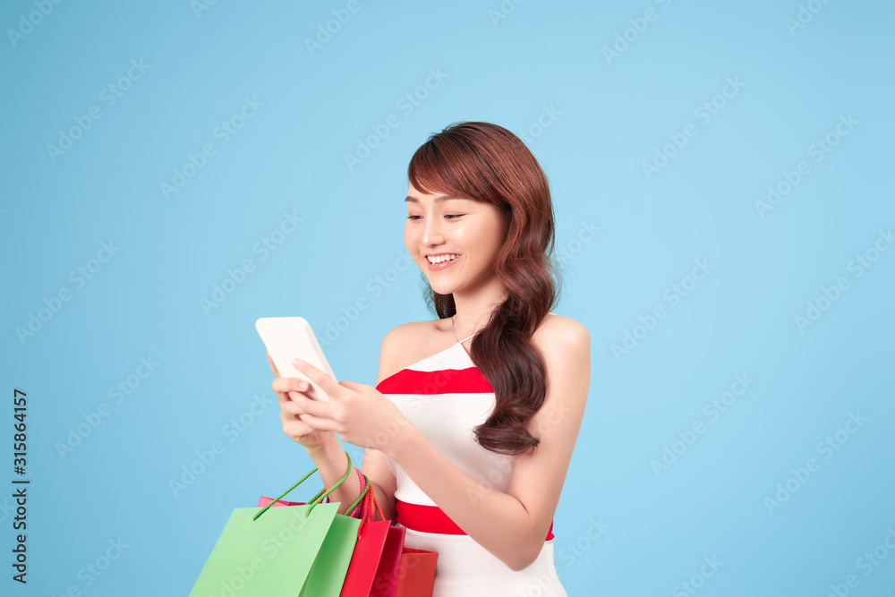 Beautiful young woman is using a smart phone for shopping online isolated on blue background studio