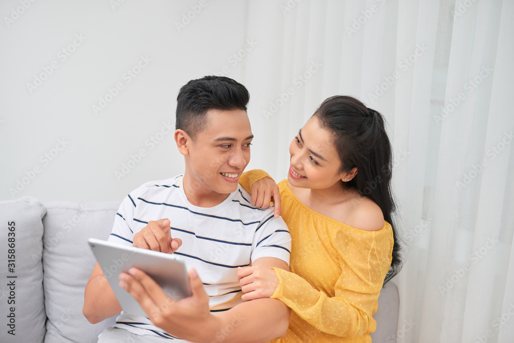 Happy young couple sitting on sofa and using digital tablet. Online shopping concept.