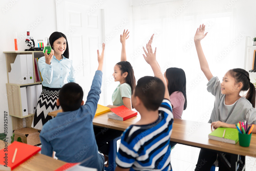 亚洲学生在教室里和老师一起学习，亚洲老师站着用手扶烧瓶