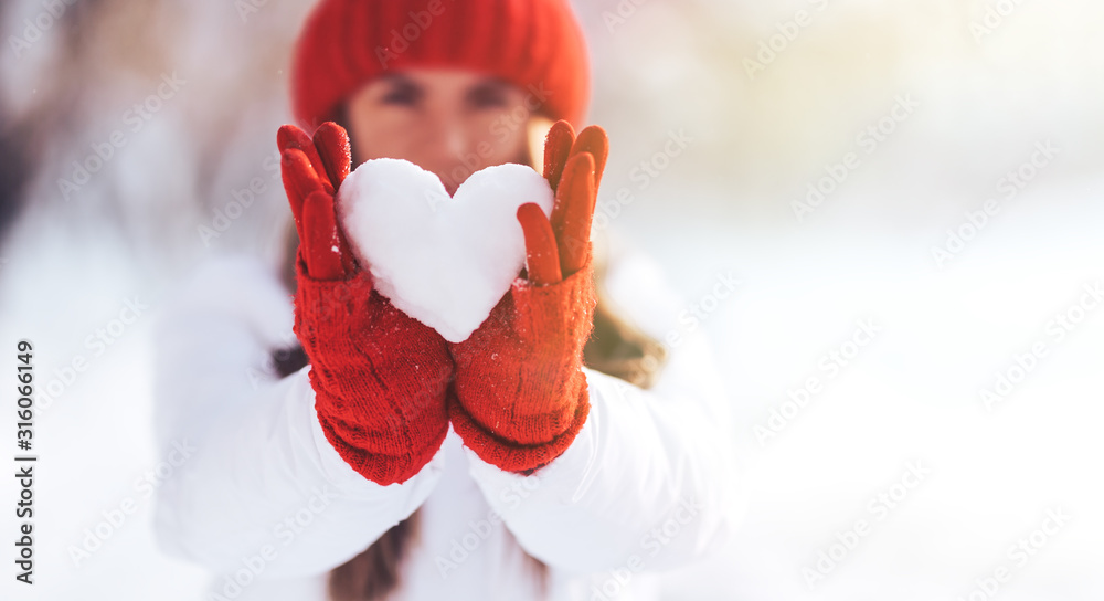 戴着红手套和帽子的女人，在雪地里保持着心形，情人节，日落。爱情概念。