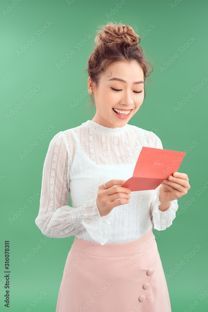 Smiling young Asian woman reading letter while standing green background.