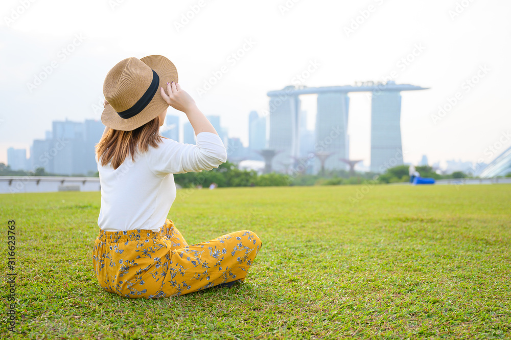 新加坡度假时，一名年轻的亚洲女子坐在滨海公园，背景是滨海湾