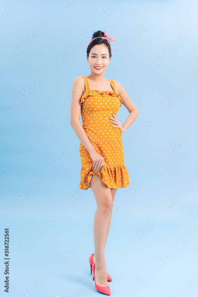 Beautiful young woman in polka dot dress is standing, looking away and smiling