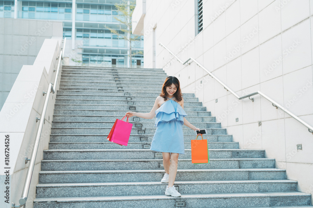 现代亚洲女孩下楼拿着购物袋。购物狂的概念。