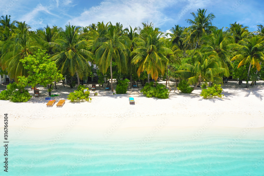 Beautiful white sandy beach with turquoise ocean water, waves, green fluffy palm trees and blue sky 