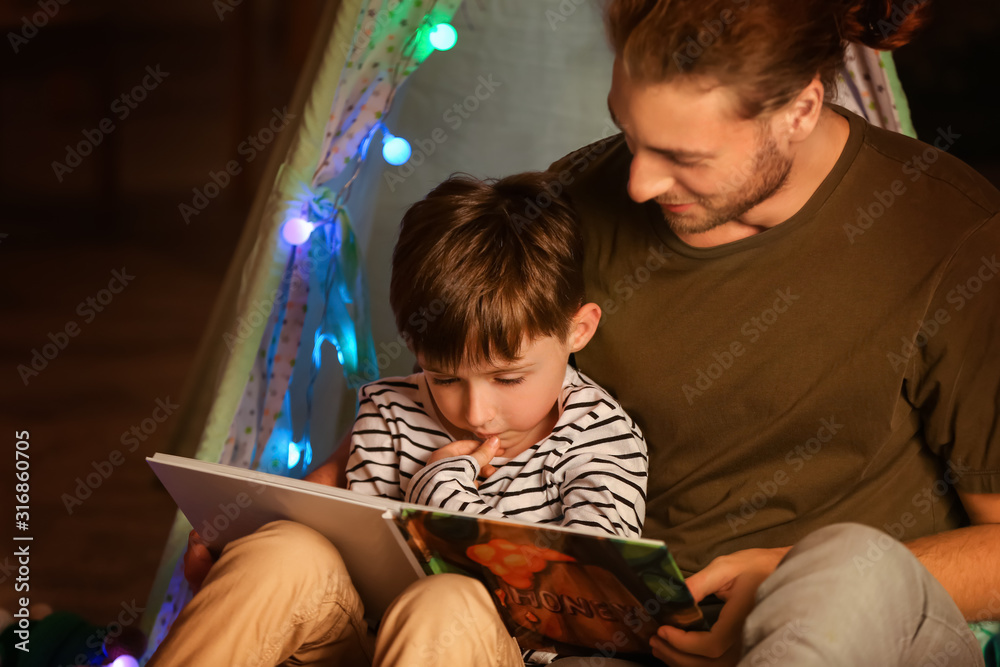 Father and his little son reading book at home in evening