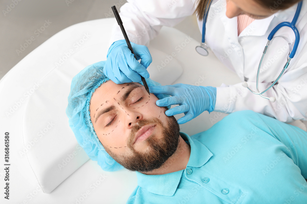 Plastic surgeon applying marks on patients face in clinic