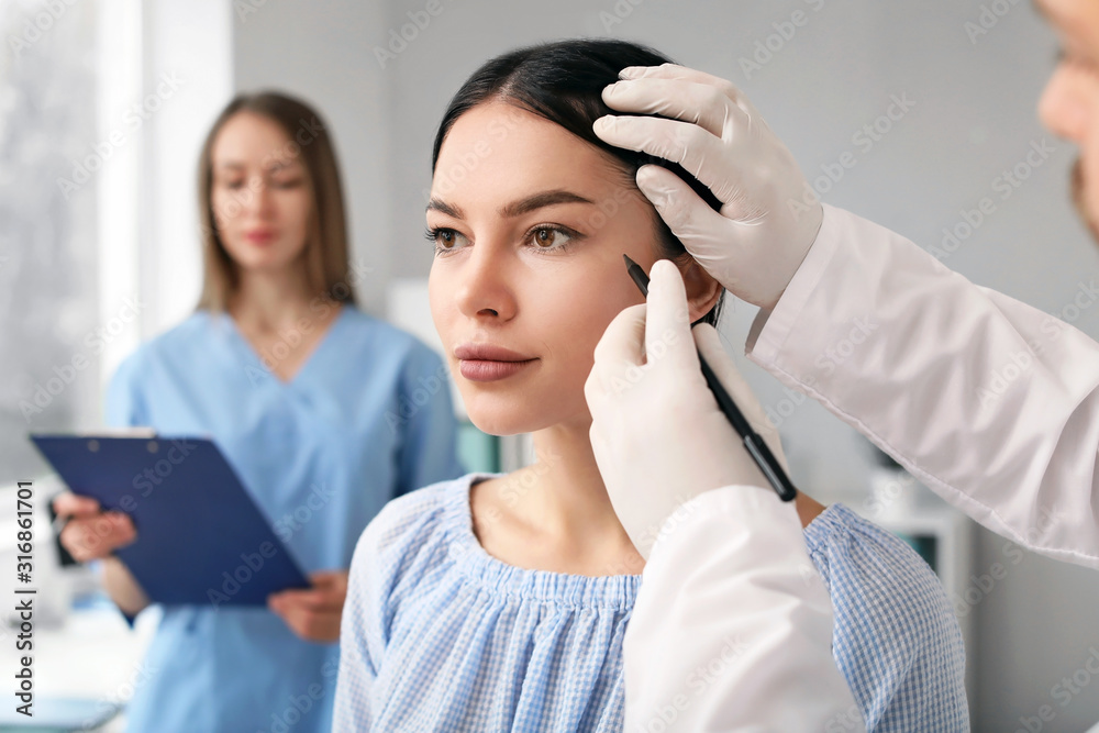 Plastic surgeon applying marks on patients face in clinic