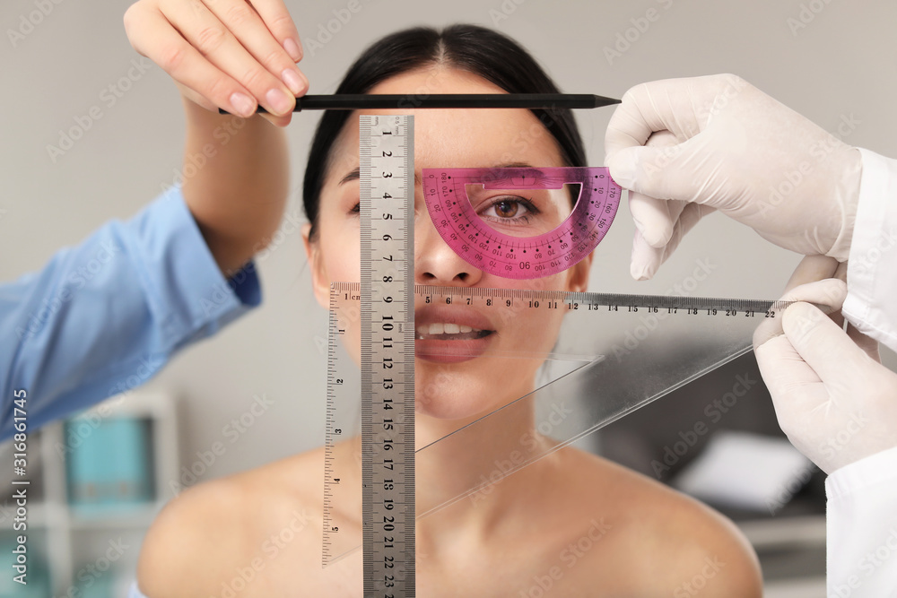 Plastic surgeon with assistant examining young womans face prior to operation in clinic