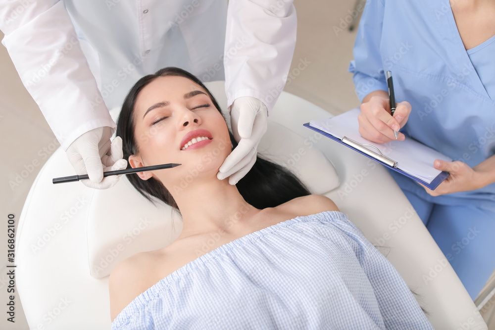 Plastic surgeon applying marks on patients face in clinic