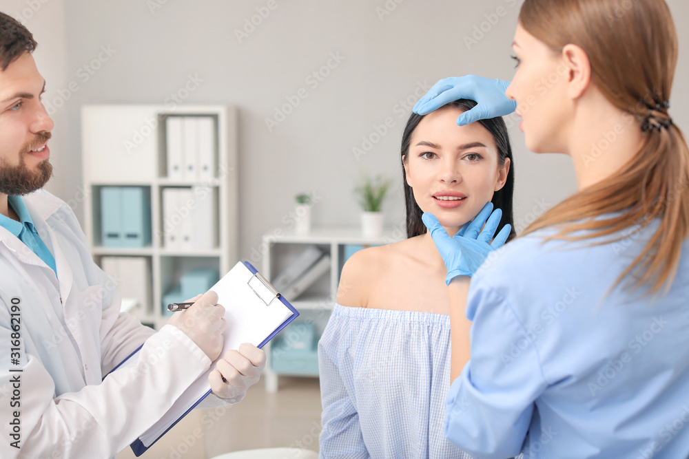 Plastic surgeon with assistant examining young womans face prior to operation in clinic