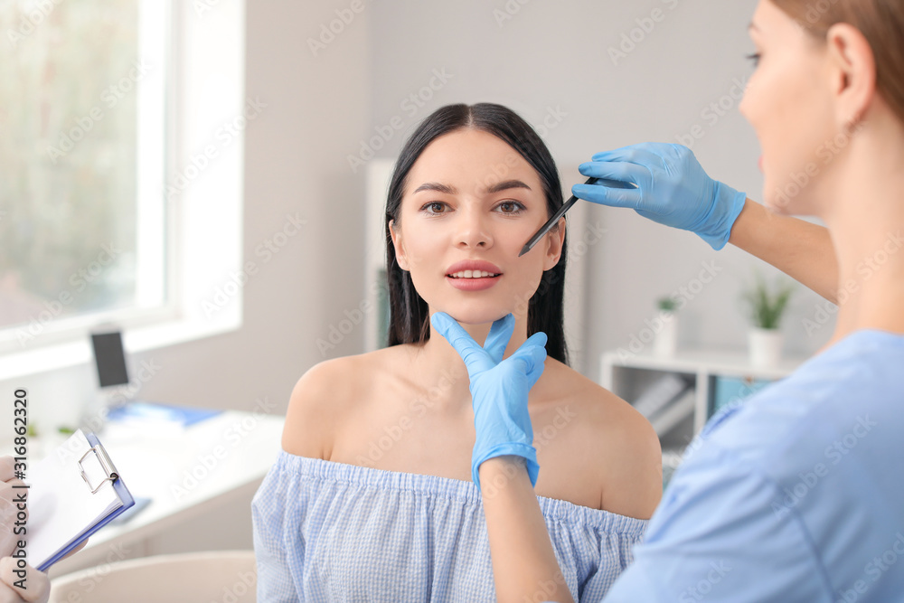 Plastic surgeon applying marks on patients face in clinic