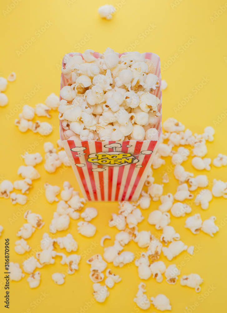 Butter popcorn in a red popcorn cup, snack in the house or cinema on a yellow background