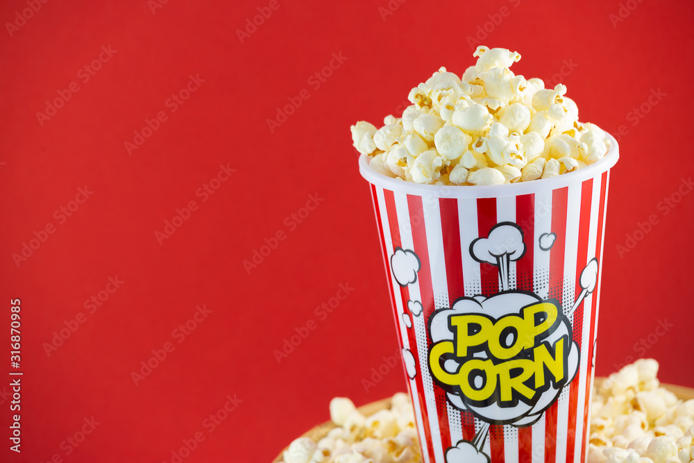 Butter popcorn in a red popcorn cup, snack in the house or cinema on a red background