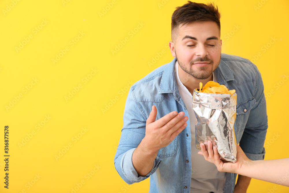 Handsome young man and hand with tasty potato chips on color background