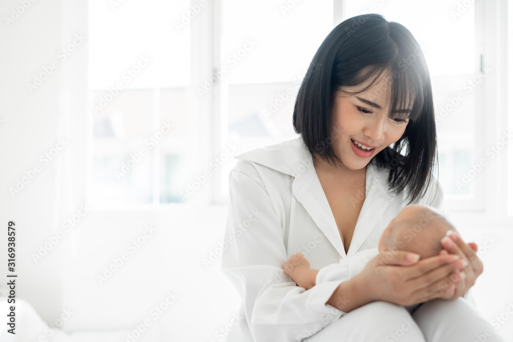 Young Asian mother holding her newborn baby with love on white bed, mothers day concept