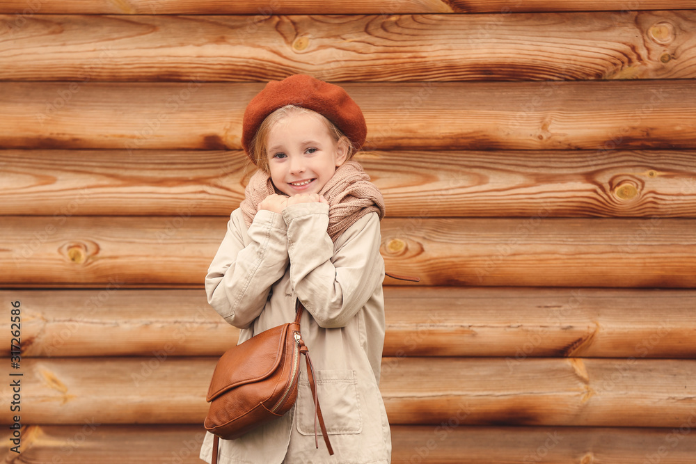 Cute little girl in autumn near wooden wall outdoors