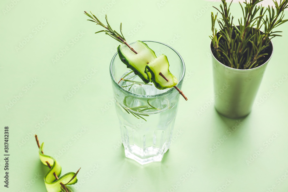 Glass of cold cucumber water on color background